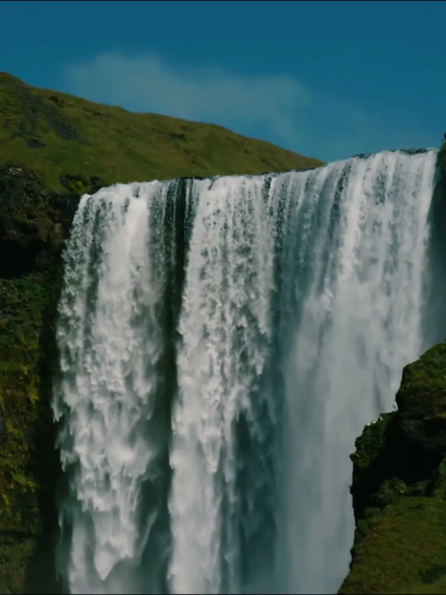 A tall waterfall pouring between green, mossy cliffs under a blue sky